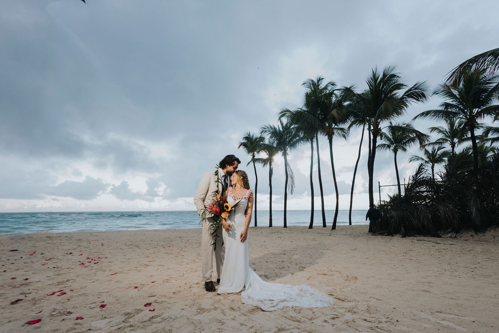 Dramatic wide portrait of the couple beneath palms and a stormy Caribbean sky