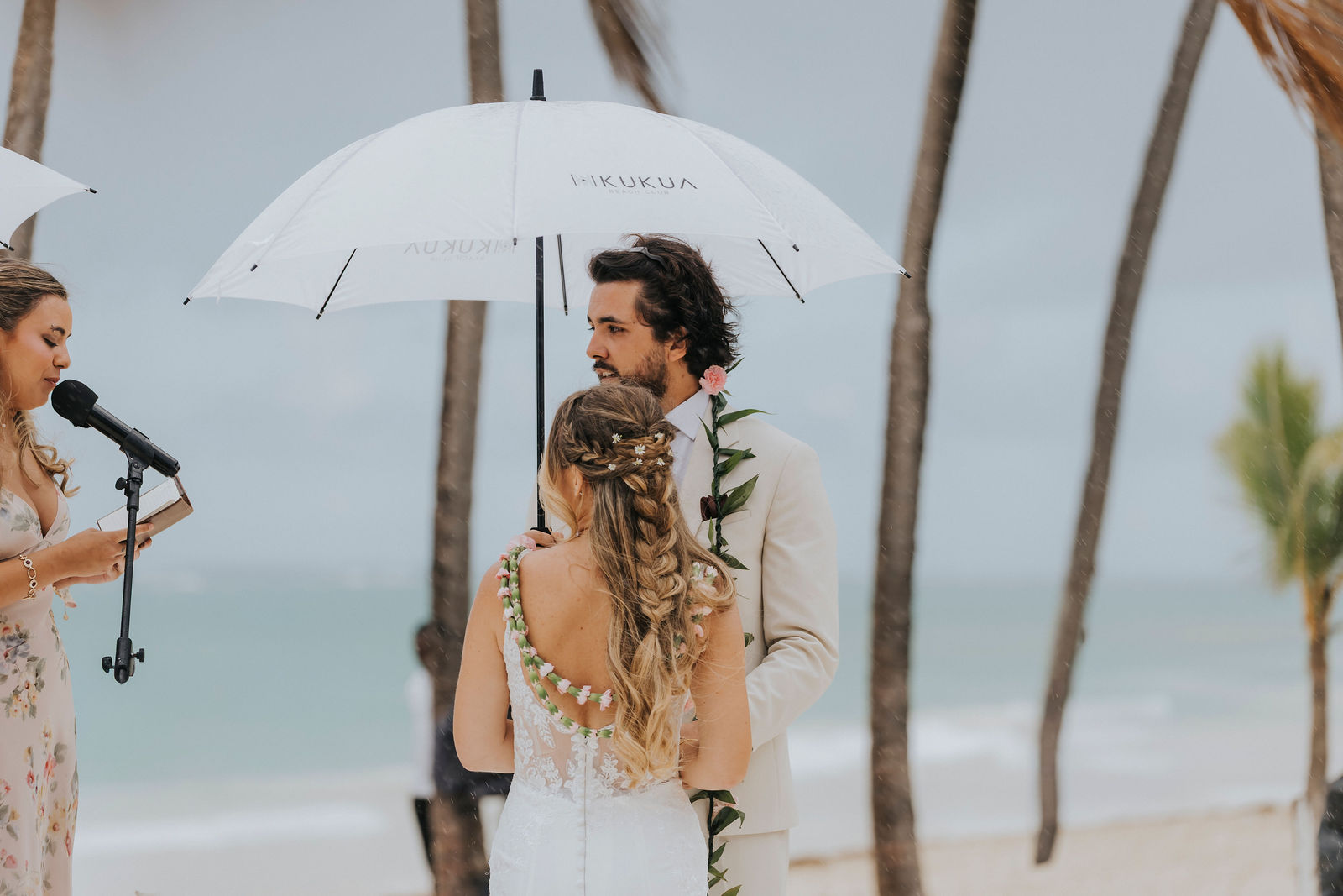 Bride and groom beneath white umbrellas during a tropical rain shower