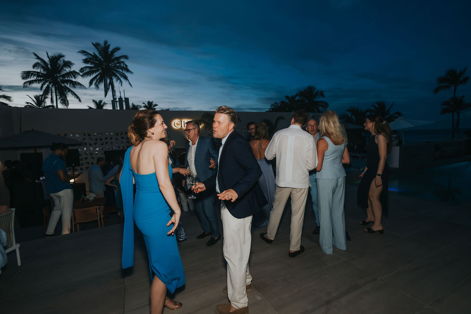 Wide blue-hour frame of the celebration with palms and open sky