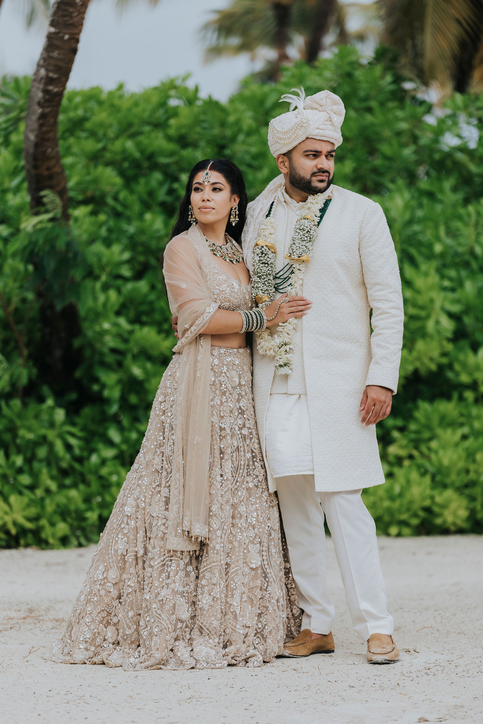Full-length portrait of the couple in Indian wedding attire by tropical greenery