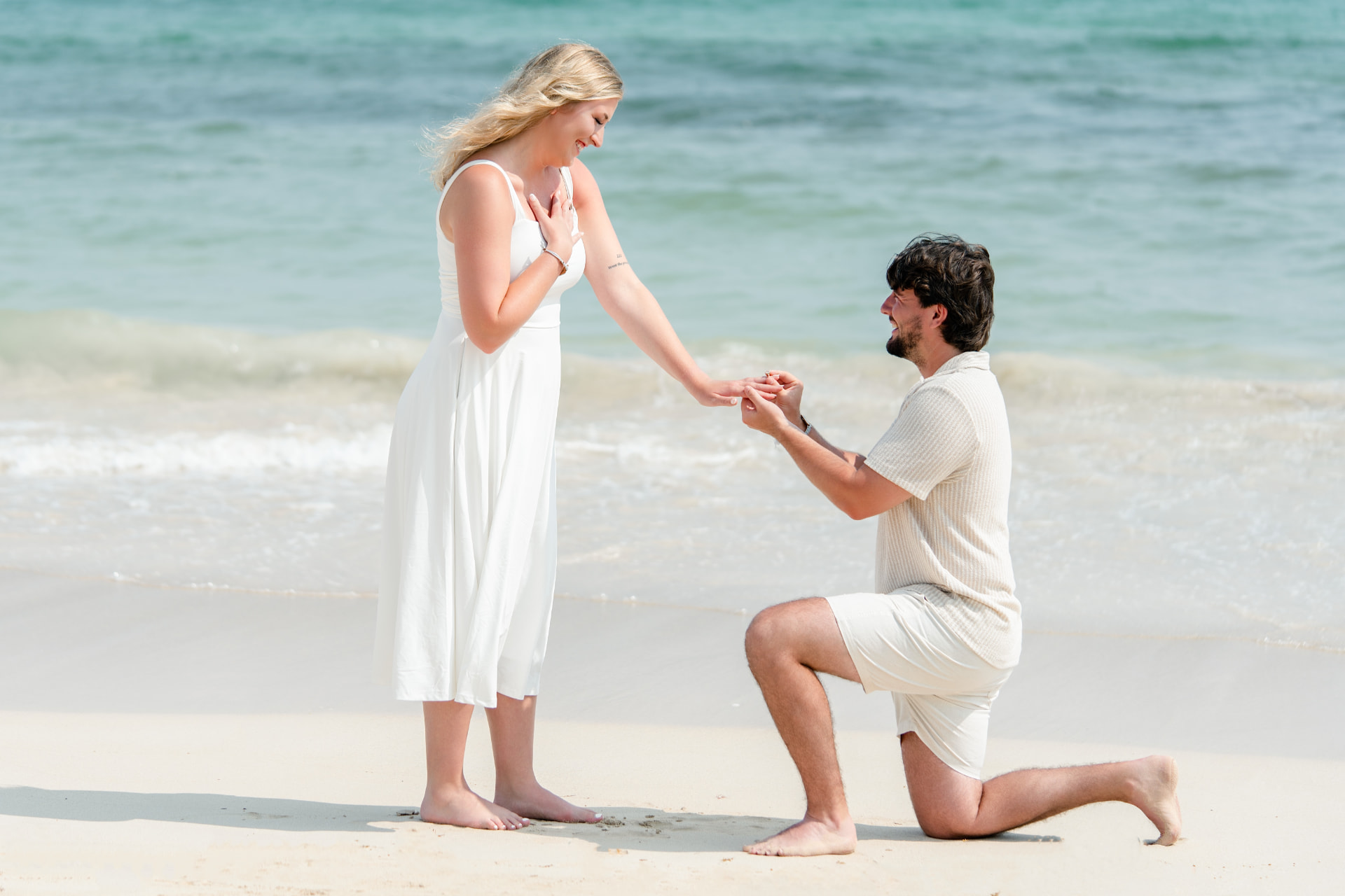 Man kneeling on a Punta Cana beach proposing to a woman in a white dress