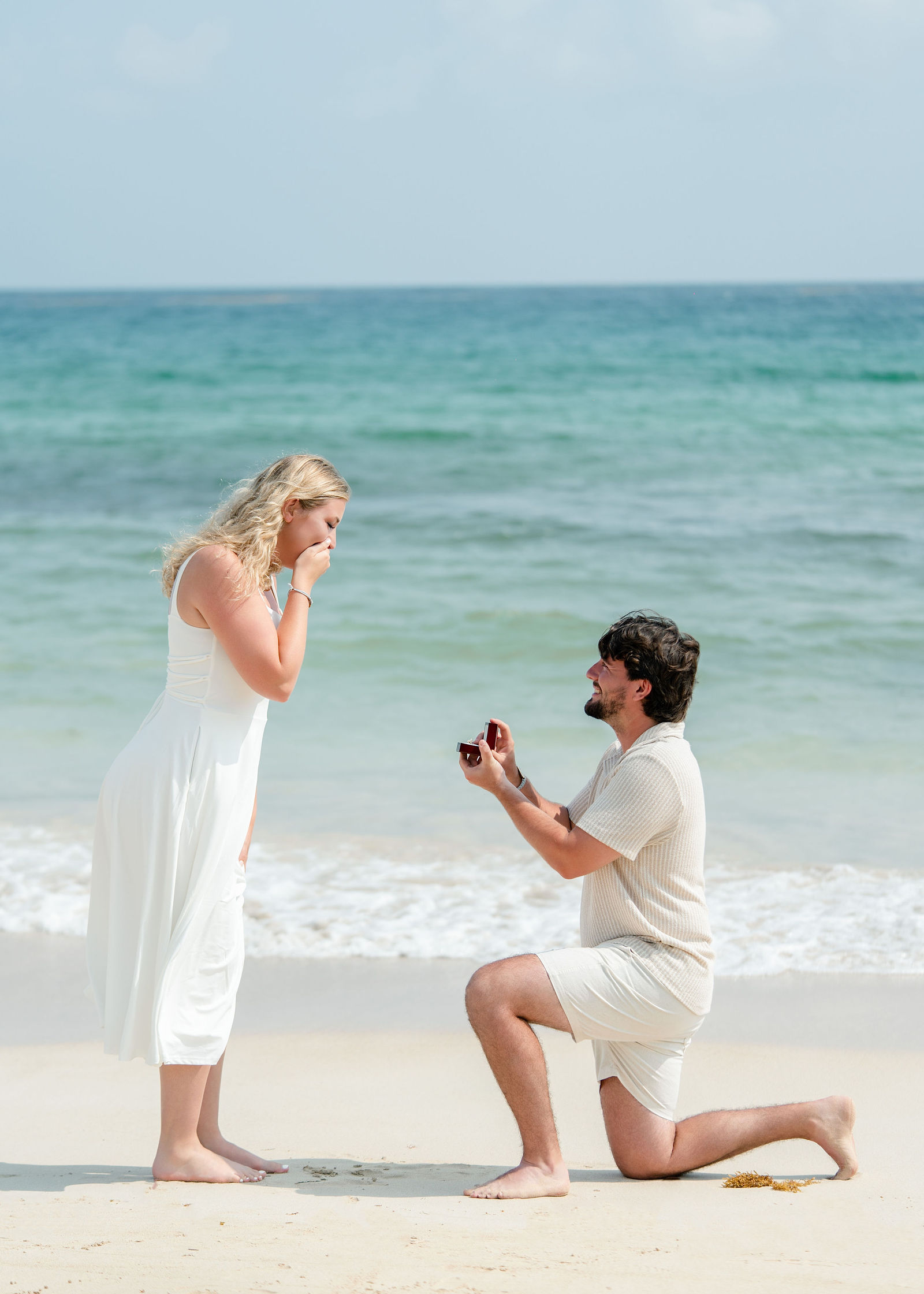 Greg on one knee proposing to Jessica at the edge of the Caribbean sea