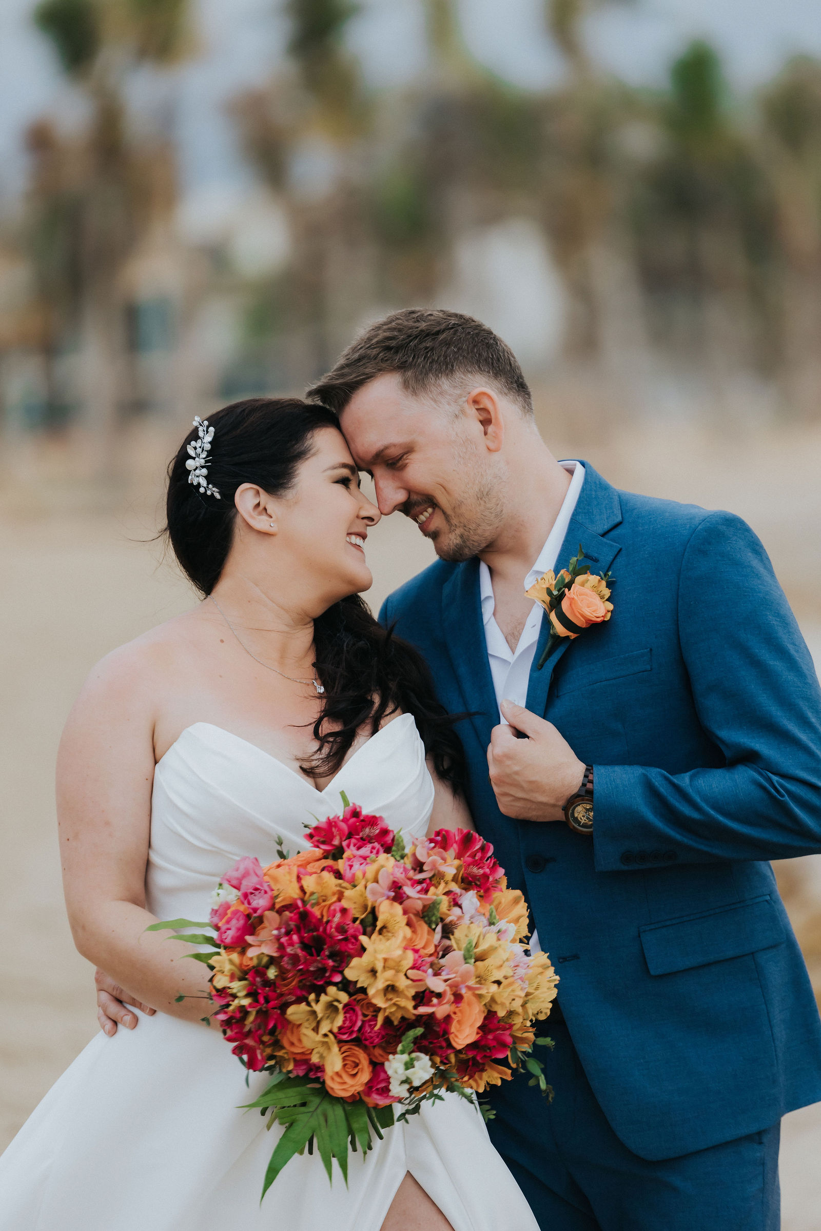 Bride and groom forehead to forehead with a vivid tropical bouquet