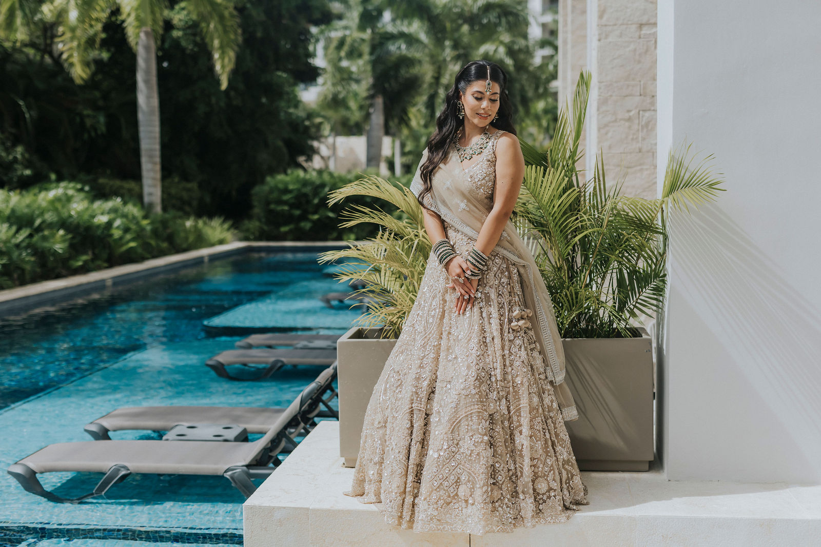 Indian bride standing beside the resort pool in a beaded ivory lehenga