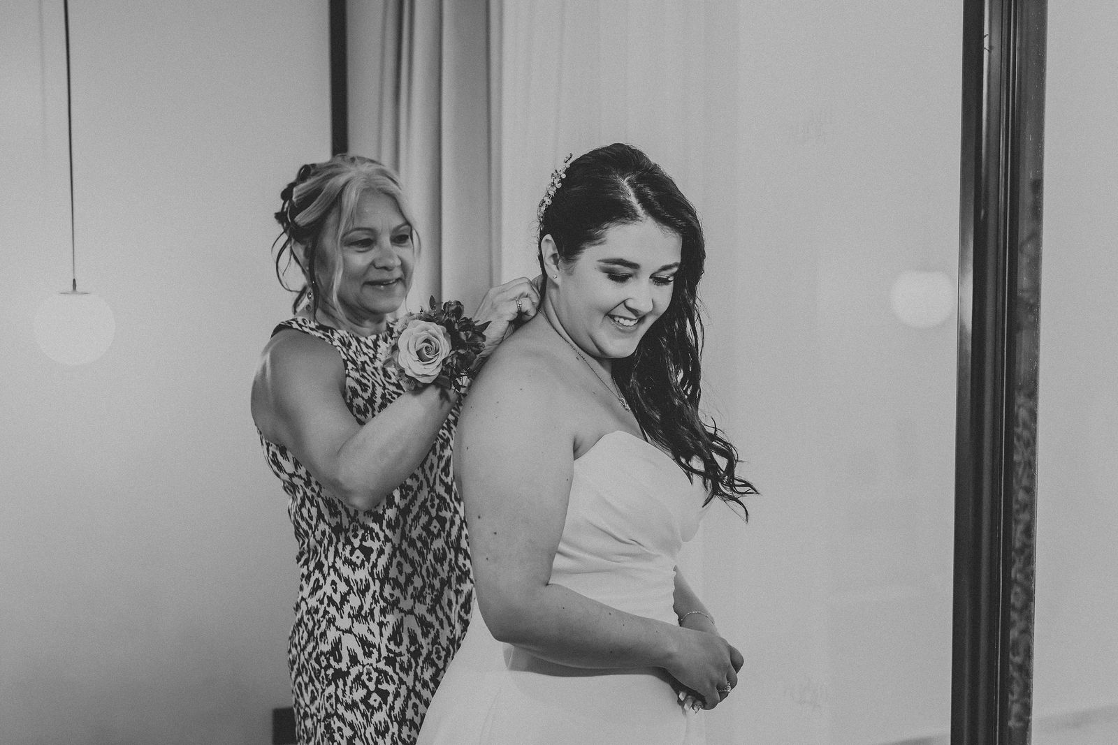 Black and white candid of the bride being helped into her gown