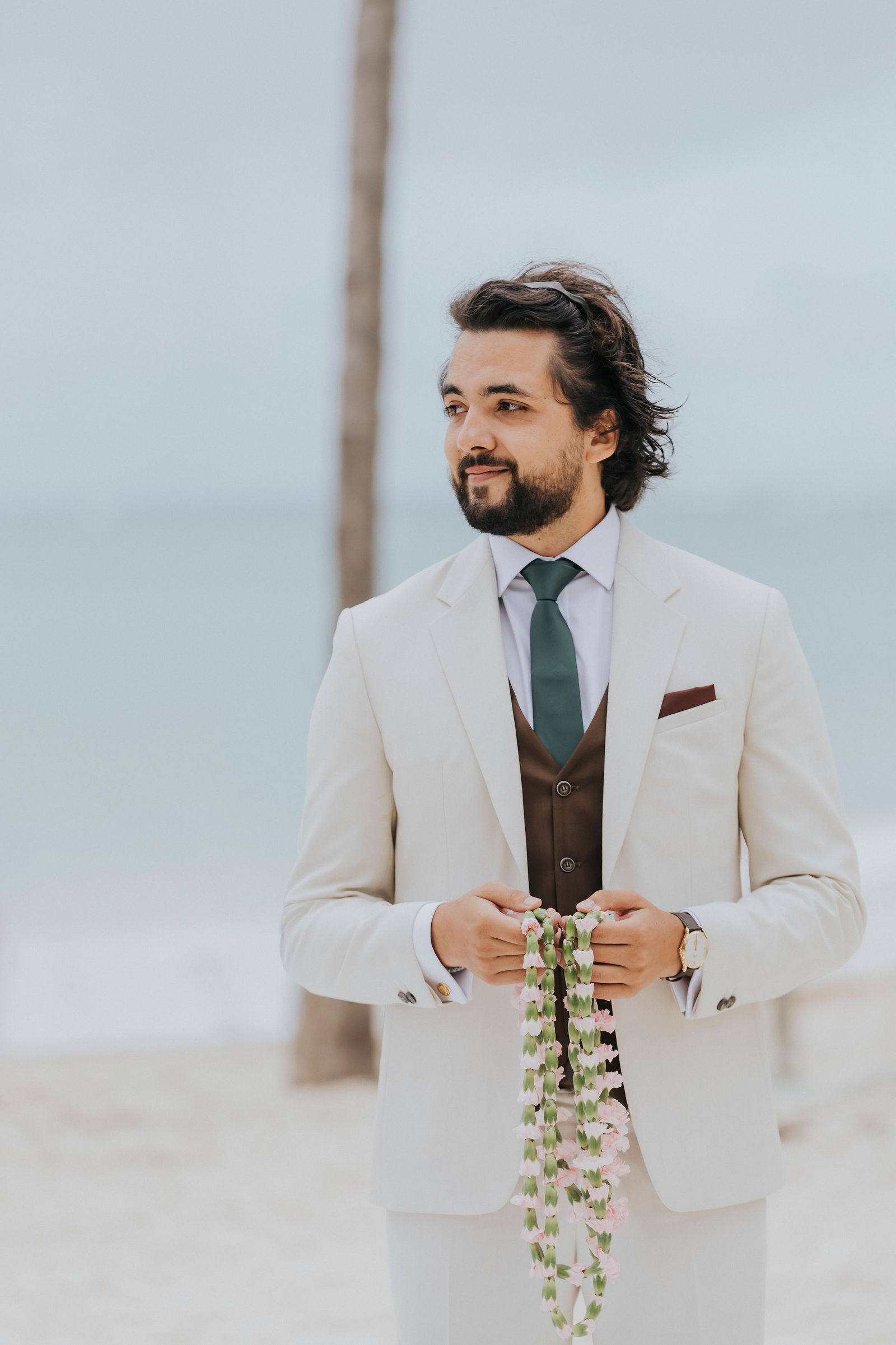Groom in an ivory suit with a floral lei on the beach